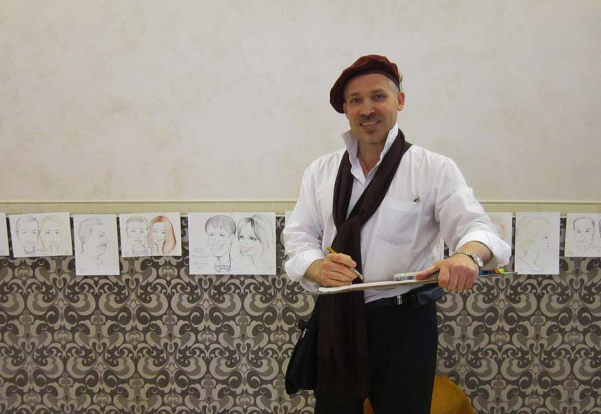 шаржист стоит на фоне своих шаржей в линию Минск 